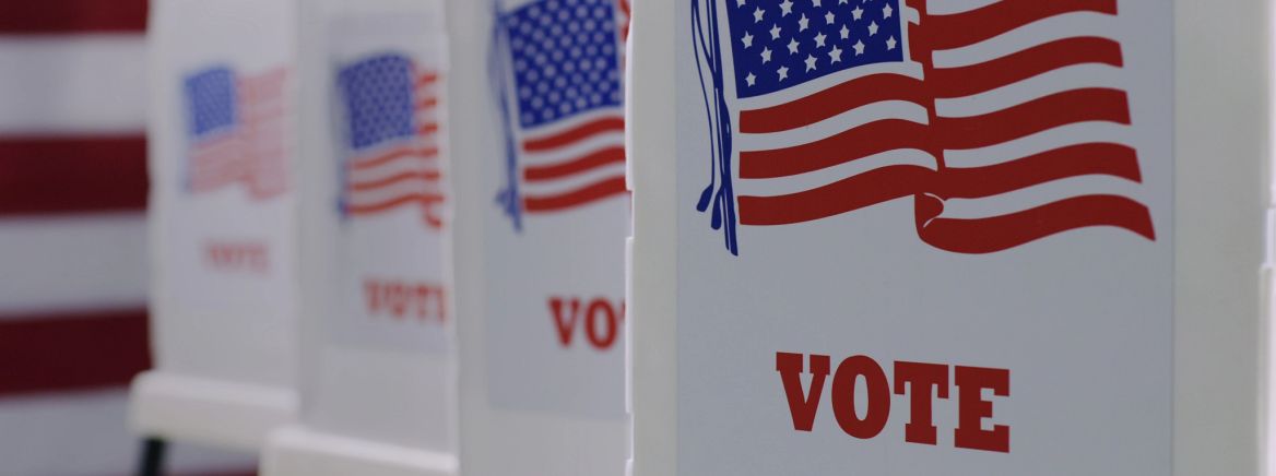 straight row of voting booths at polling station during American election. US flag in background.