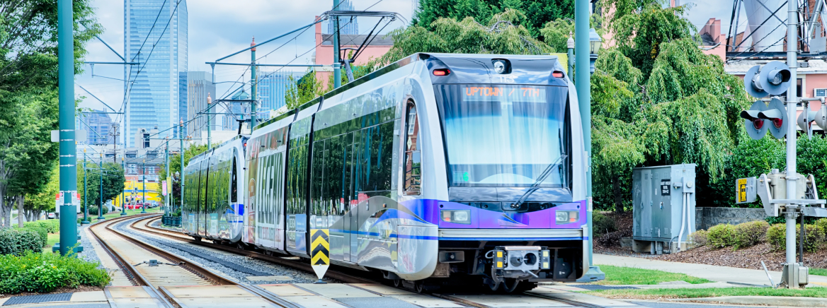 A Charlotte light rail traveling south with the Charlotte skyline in the background